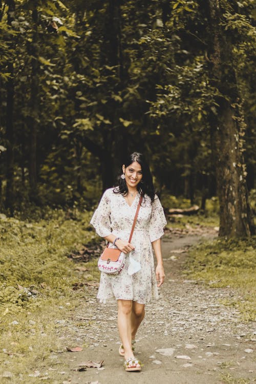 A Smiling Woman in Floral Dress Walking on Forest Path