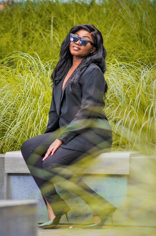 A Woman in Black Blazer and Pants Smiling while Sitting on a Concrete Bench