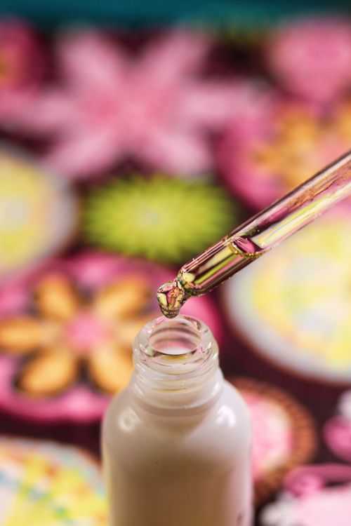 Free CBD oil dropper close-up with colorful floral background, showcasing product detail and beauty. Stock Photo