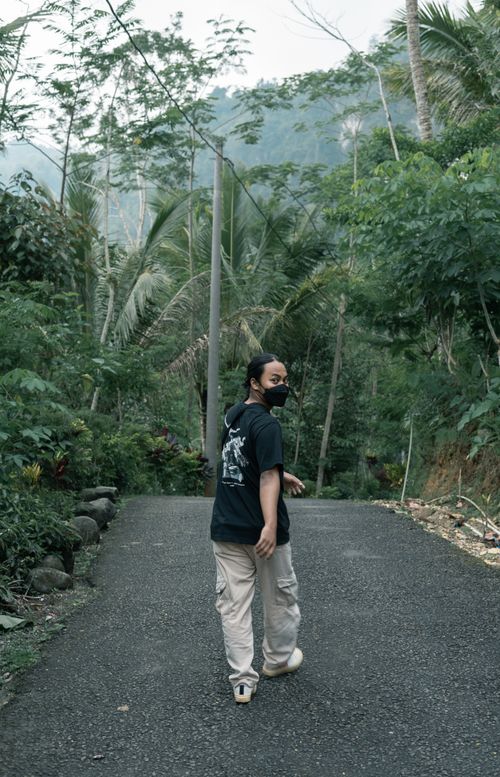 Free A person walking on an asphalt path surrounded by lush greenery, looking back. Stock Photo
