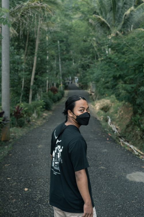 Free A person wearing a mask walks along a lush forest pathway, looking back. Stock Photo