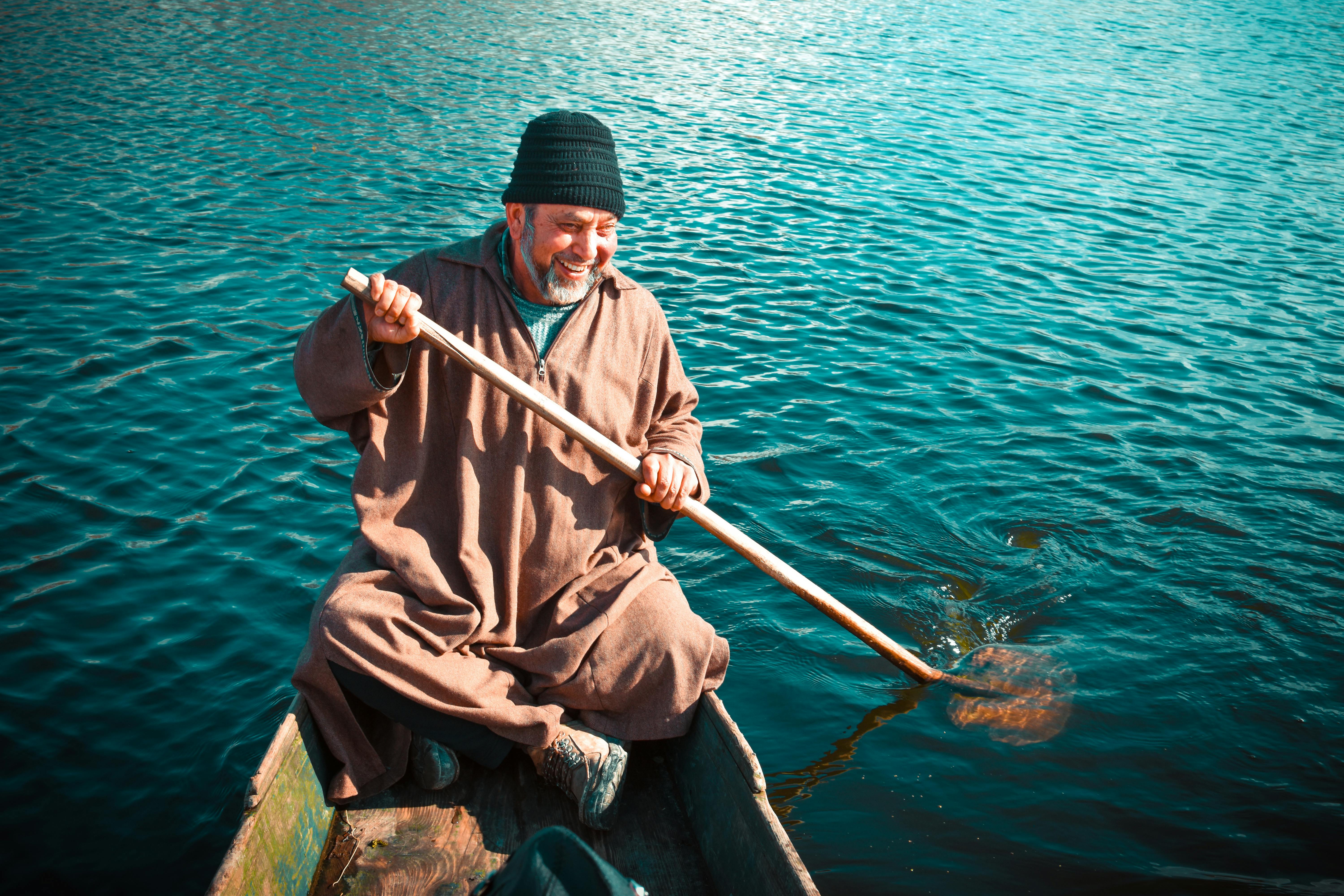 Senior man smiling while rowing a wooden boat on clear water, exhibiting joy and tranquility.