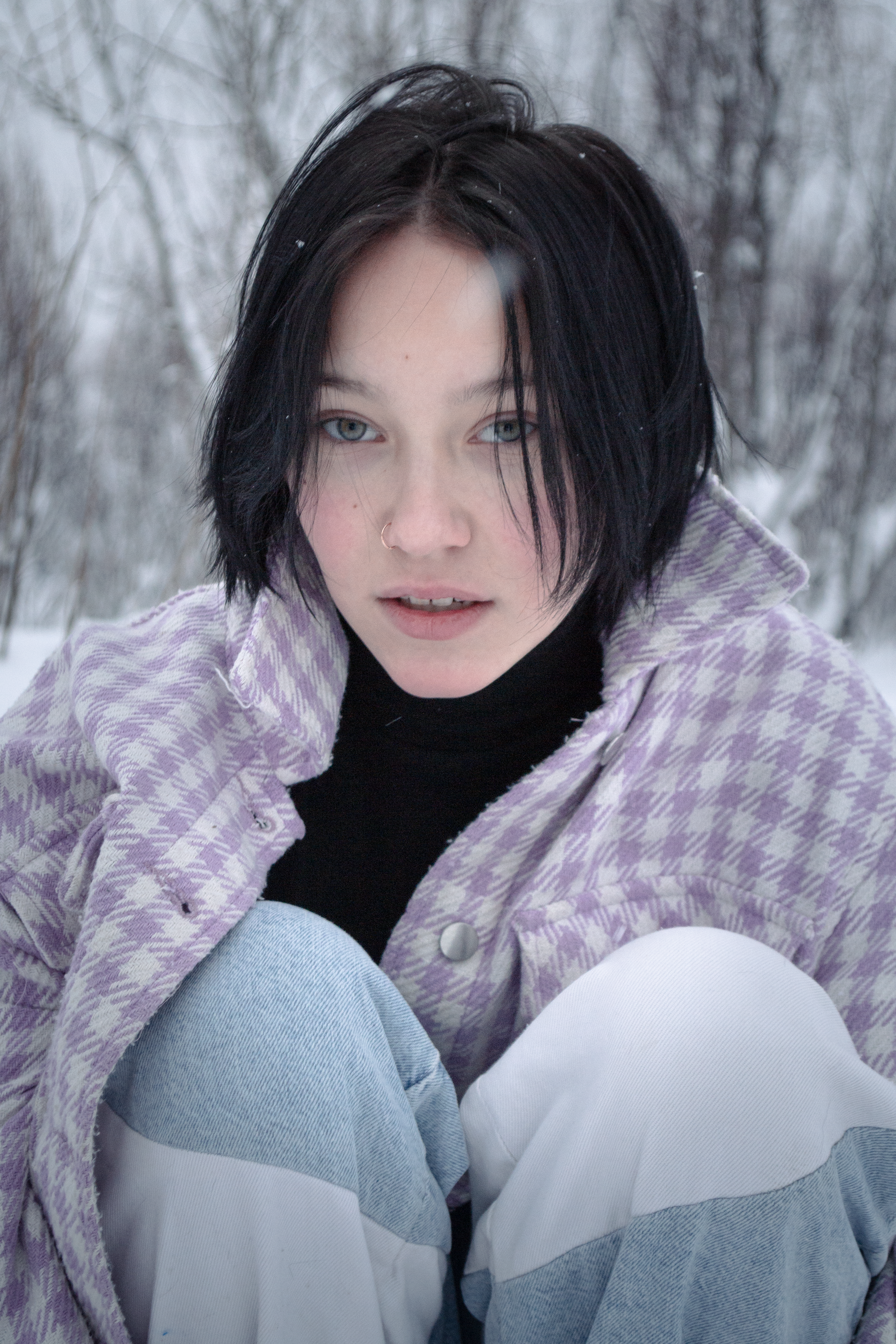 A young woman with short hair wearing a plaid jacket in a winter setting.