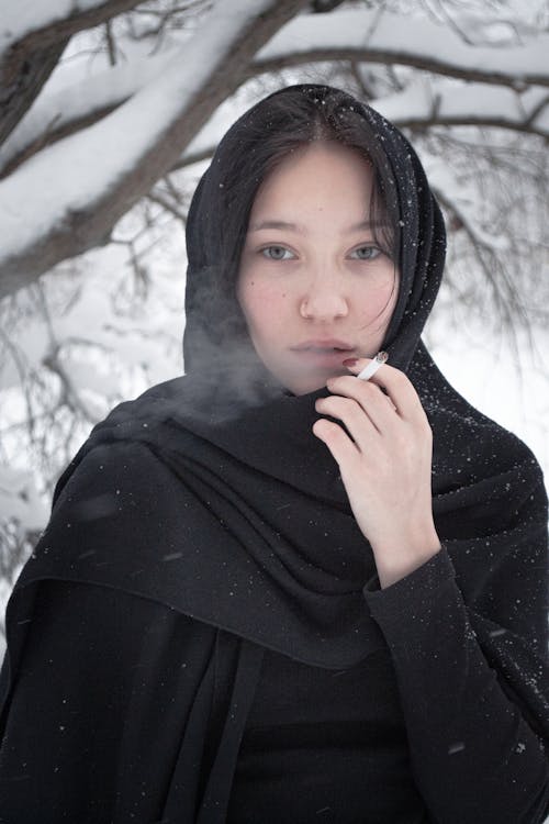 A Woman in Black Headscarf Smoking Outside