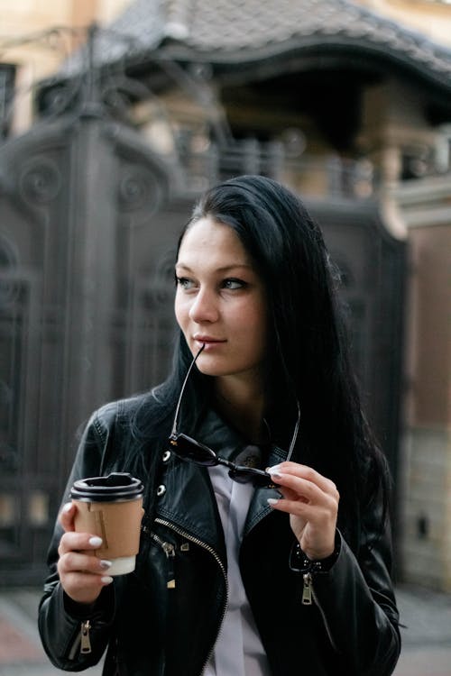 A Woman in Black Leather Jacket Holding a Disposable Cup and Sunglasses