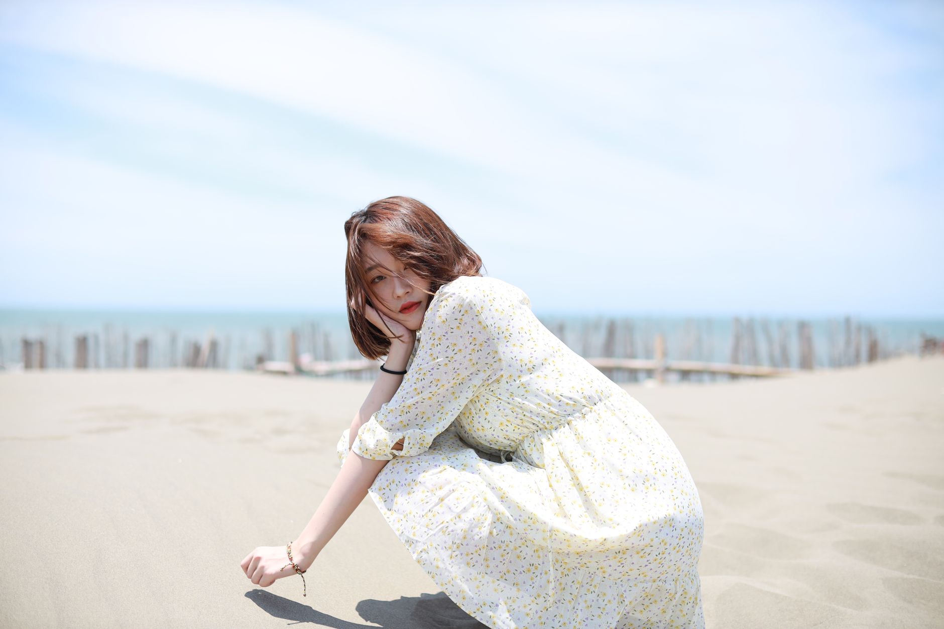 Peaceful scene of an Asian woman in a floral dress sitting on a sunny beach in Taipei City.