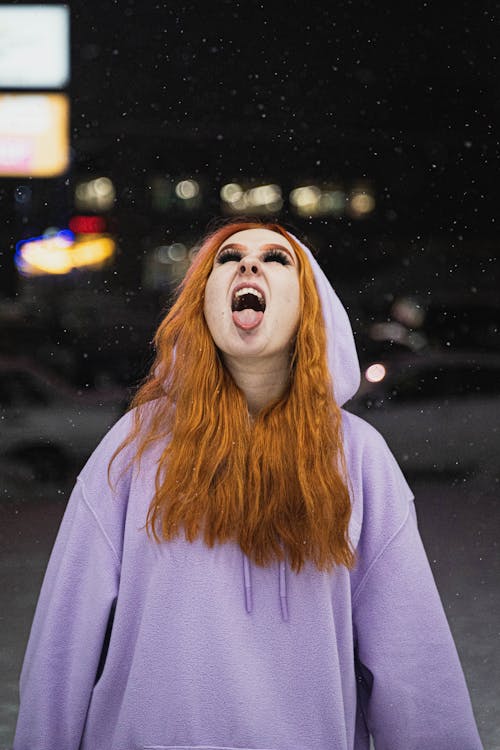 A Woman in Hoodie Sweater With Her Tongue Out while Snowing