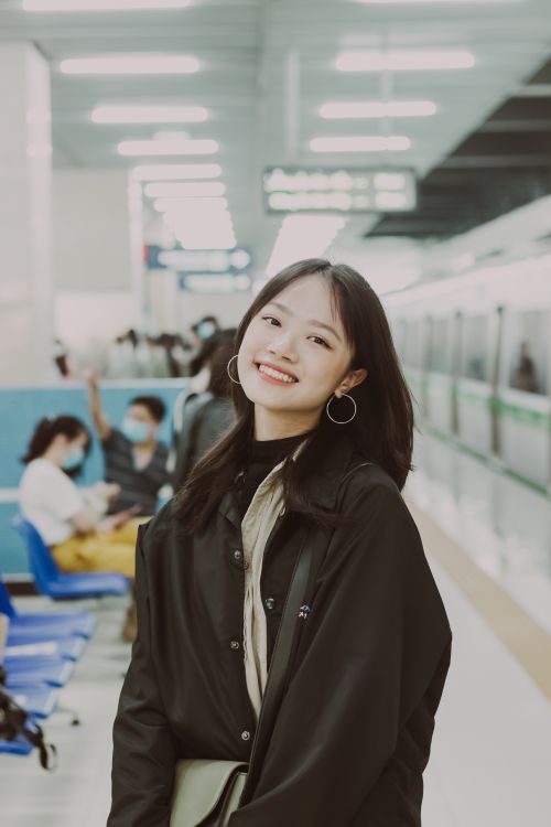 Free A young woman smiling in a bustling subway station, exuding joy and style. Stock Photo