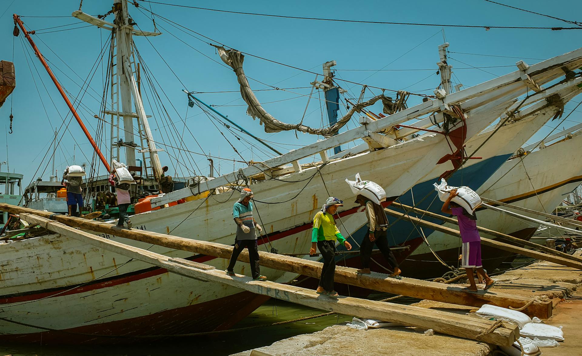 Men carrying sacks on a wooden plank to load boats at a pier in East Java, Indonesia.