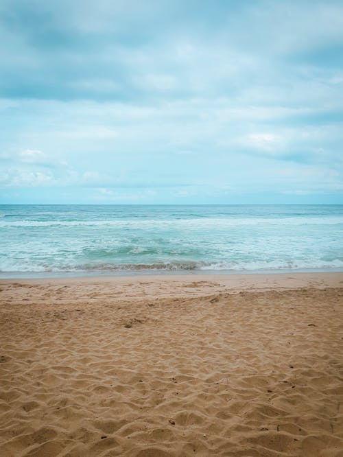 A Beach Sand Near the Sea Under the Blue Sky and White Clouds