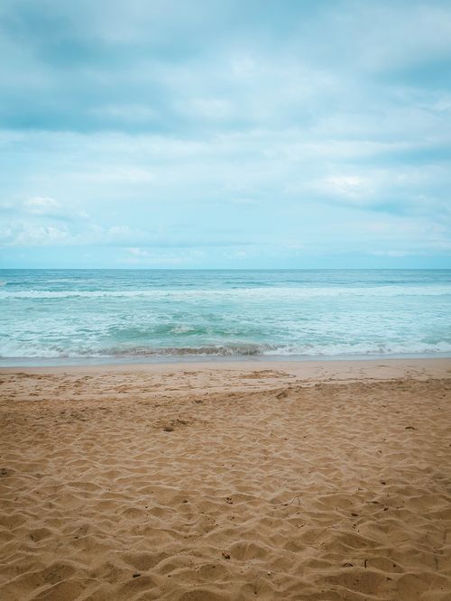 Free Peaceful ocean view with sandy beach and cloudy sky, perfect for relaxation scenes. Stock Photo