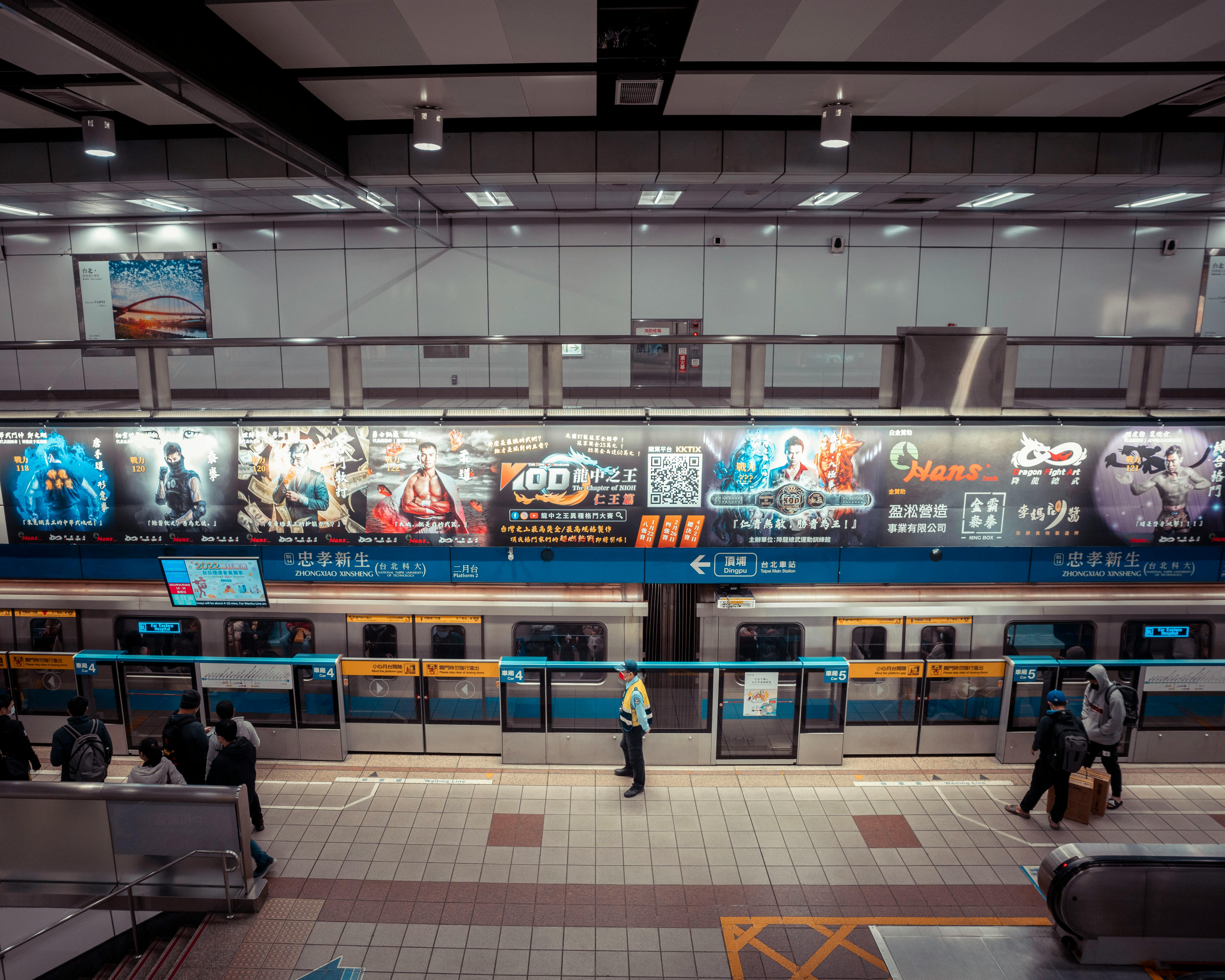 High angle view of a metro station with colorful advertisements and commuters standing and waiting.