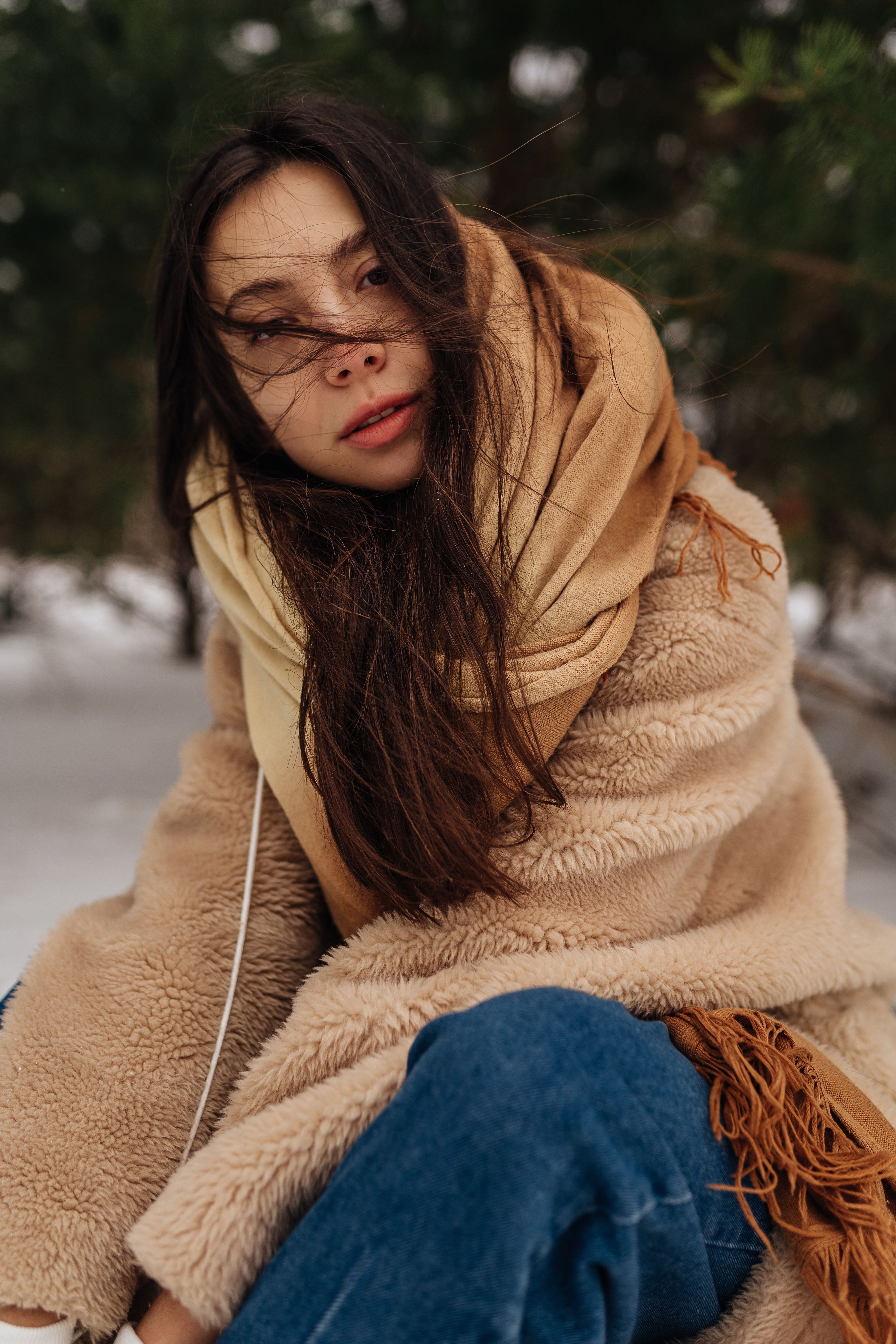 A woman with long hair sits outdoors in winter, wrapped in a coat and scarf.