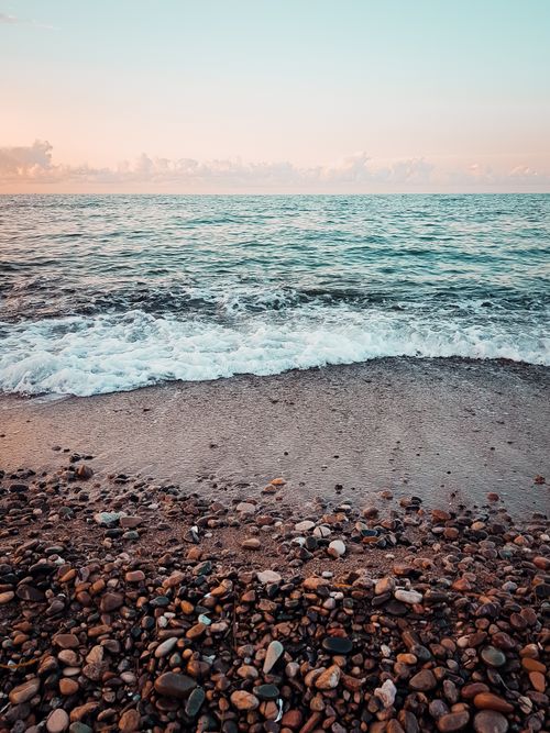 Free Peaceful pebble beach at sunset in Ordu, Turkey with soft waves and a golden sky. Stock Photo