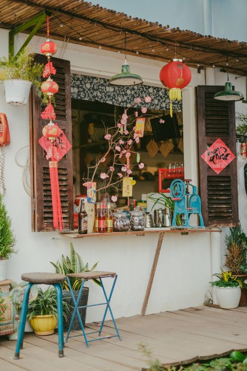 Free Cozy outdoor cafe scene with traditional red lanterns, plants, and wooden shutters. Stock Photo