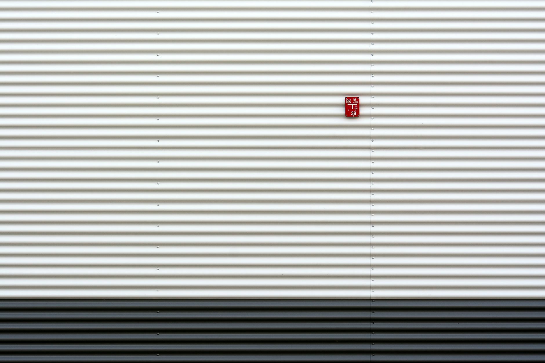 Close-up of a white corrugated metal wall featuring a small red text sign.