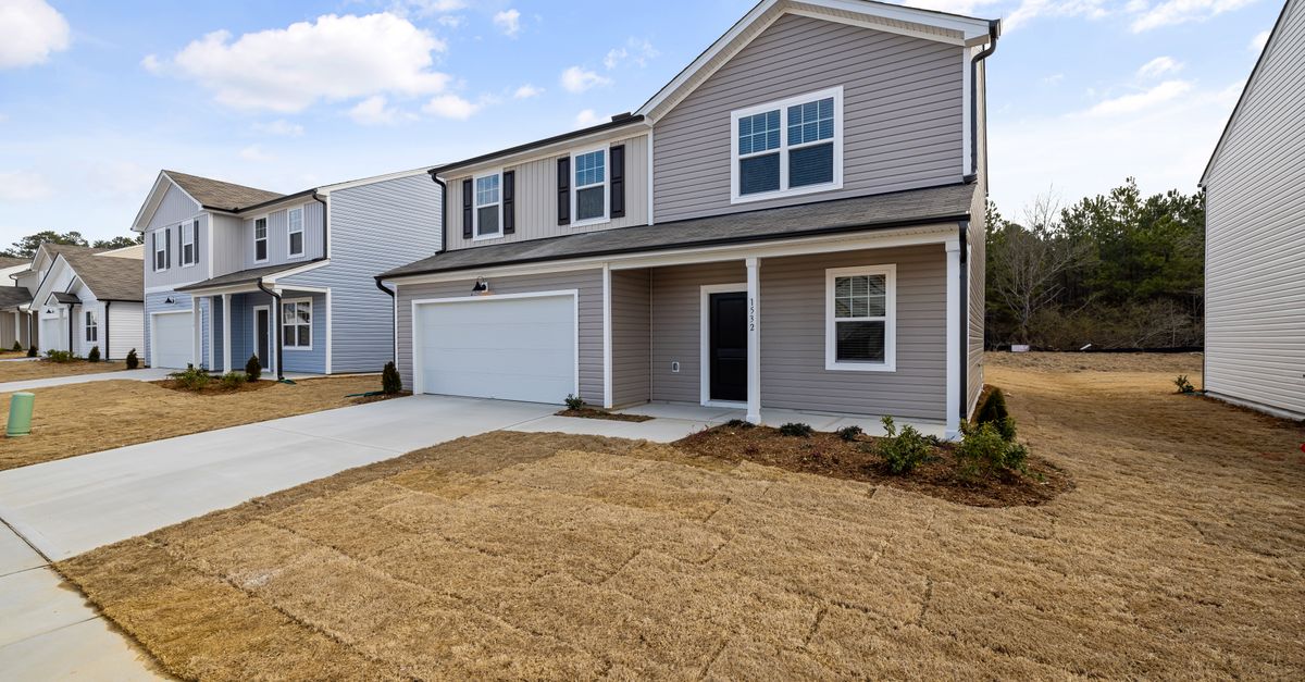 A modern suburban home with a garage, under a clear blue sky, features a dry grass lawn.