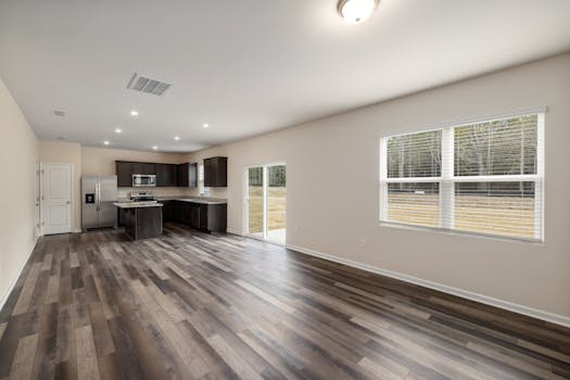 Modern open plan kitchen and living room with wooden flooring and large windows.