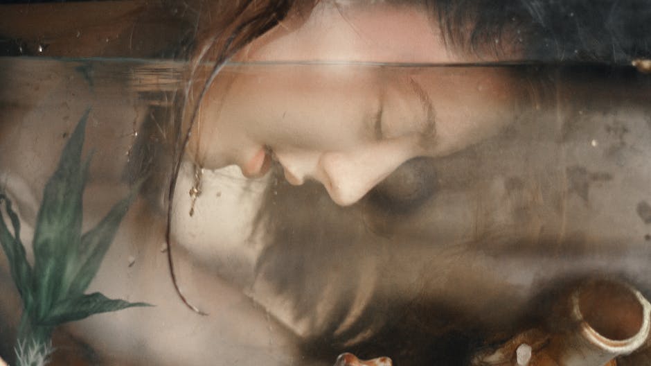 An artistic underwater photograph featuring a woman with her eyes closed and wet hair, captured in a serene pose.