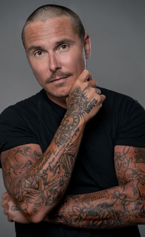 Free Portrait of a tattooed man in a black shirt with arms crossed, exuding confidence. Stock Photo