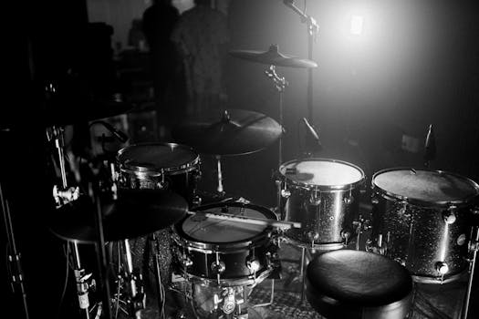 A black and white image of a drum kit set up on stage in a music venue with dramatic lighting.