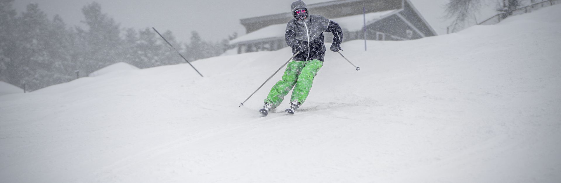 Capture of a skier in vibrant green pants skiing downhill in snowy weather.