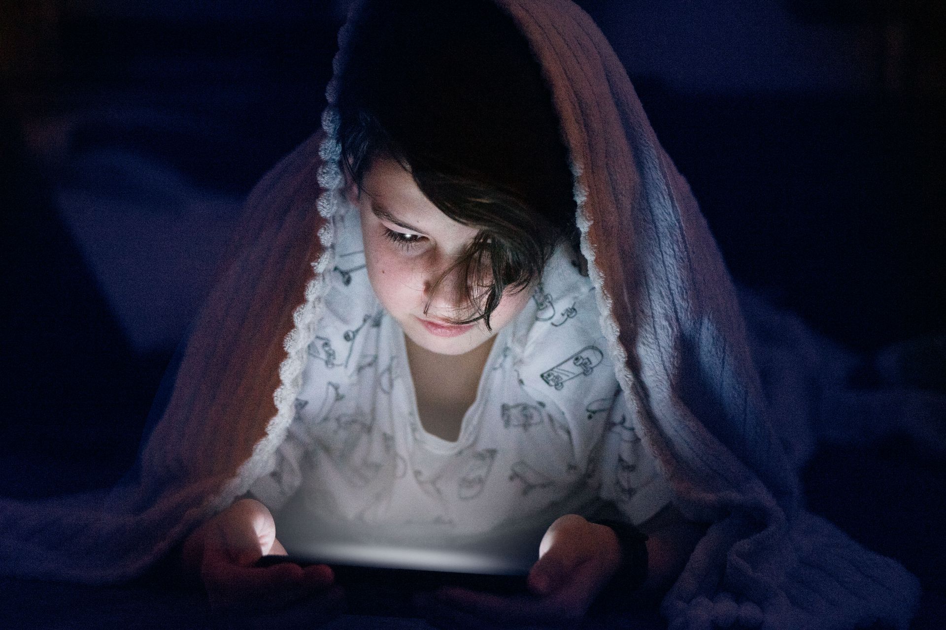 A child's face lit by the glow of a smartphone screen