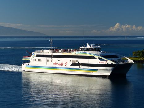 A large passenger ferry sails through calm ocean waters under a clear blue sky.