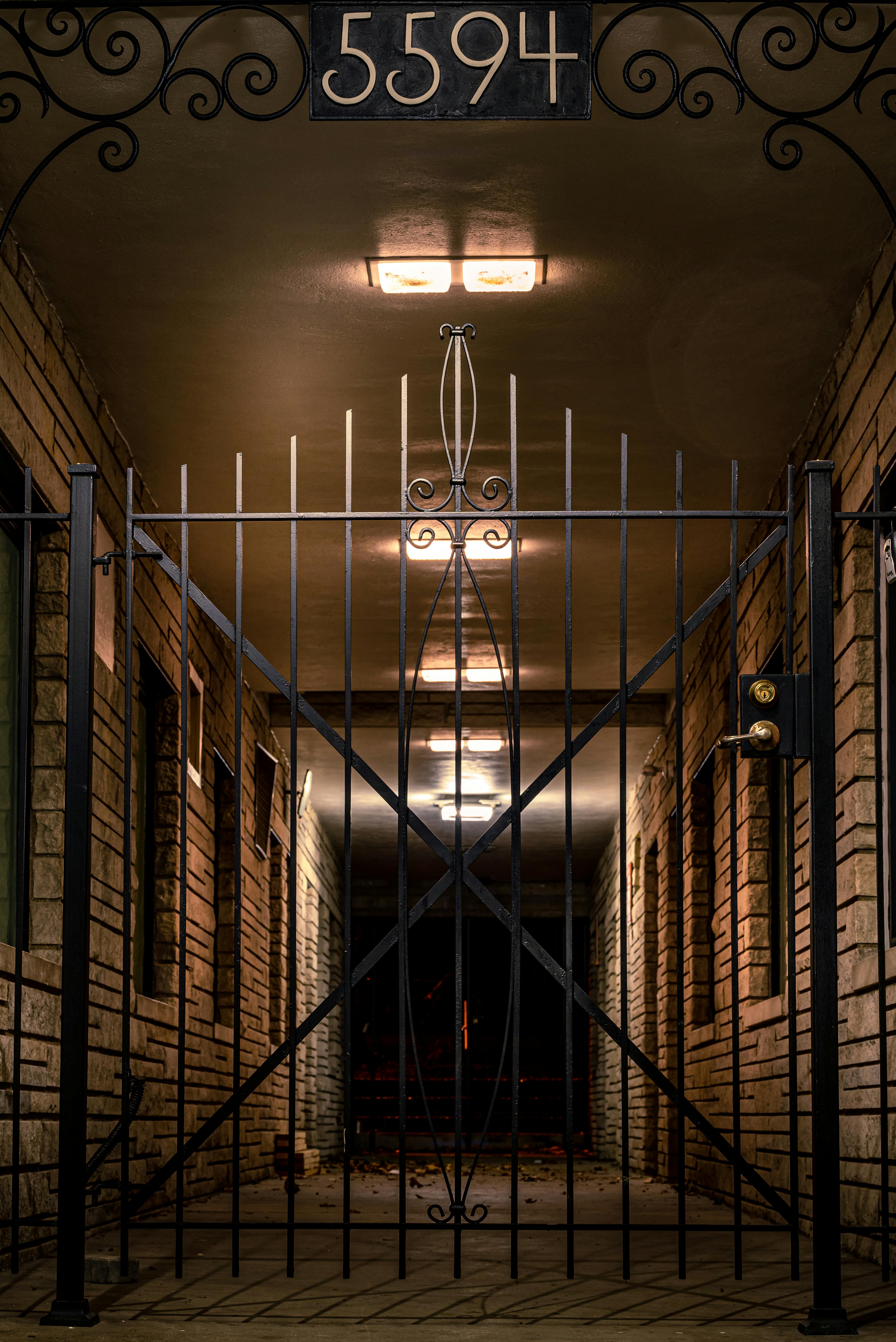 Eerie symmetrical corridor with an iron gate and illuminated brick walls creating a mysterious ambiance.