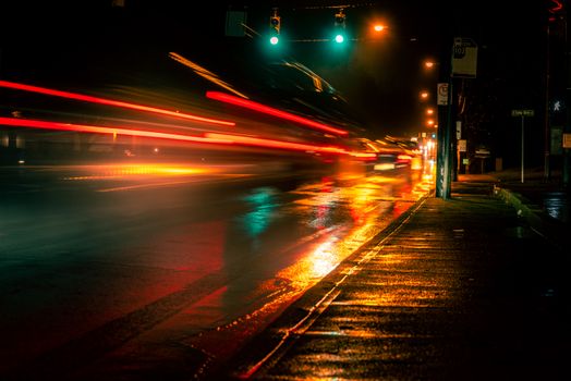 Vivid long exposure capturing blurred motion of car lights on a wet urban street at night.