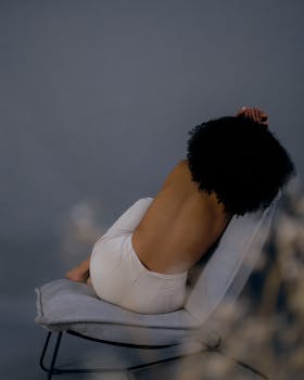 Artistic photograph of a woman posing shirtless on a chair with an elegant and moody background.