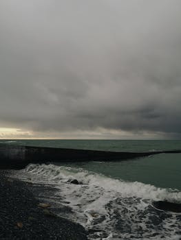 A moody seascape featuring a dark cloudy sky over an ocean horizon during the day.
