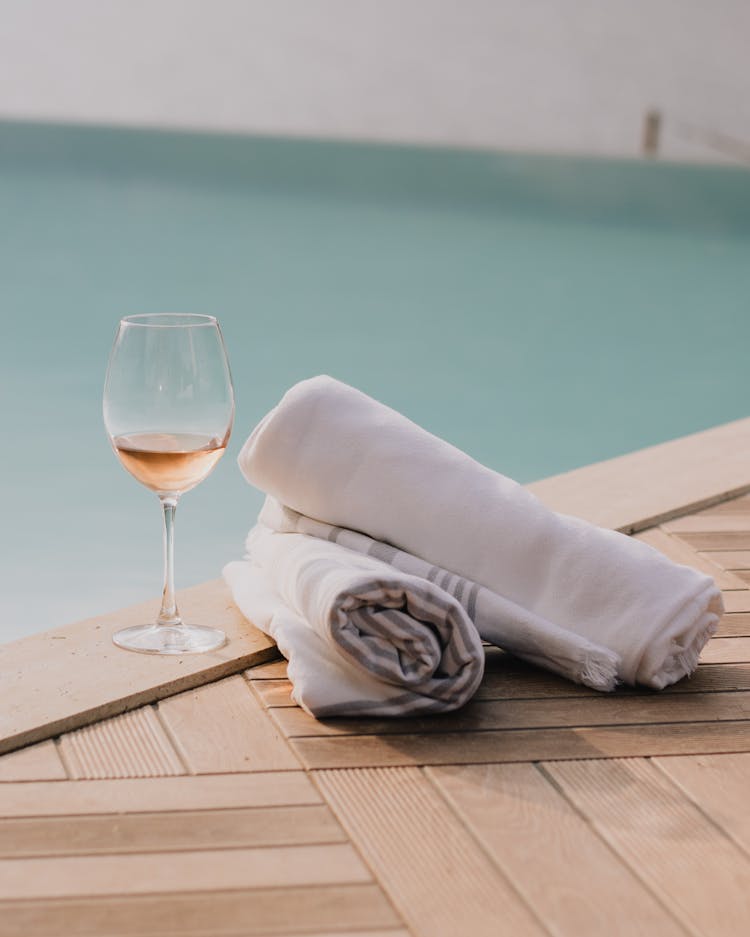 Towels And Glass Of Wine Standing On Poolside