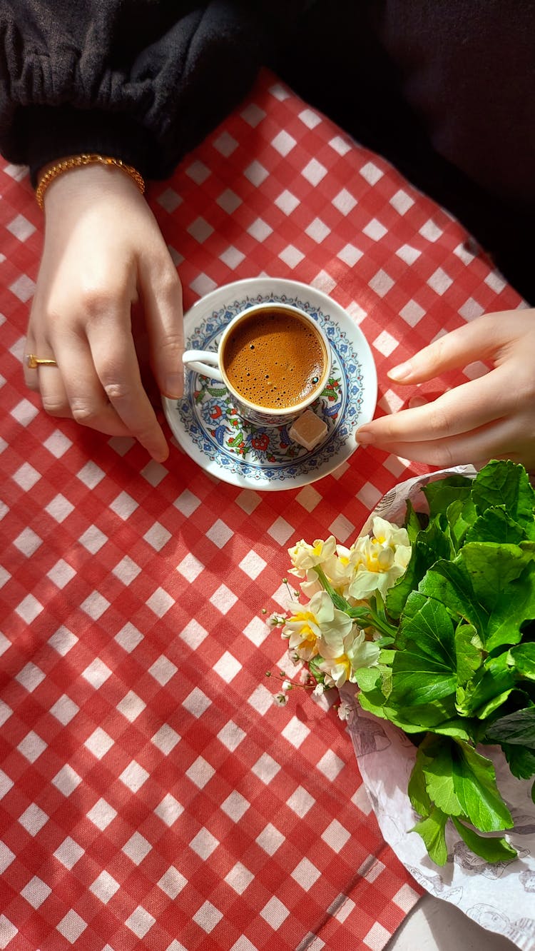 Cup Of Coffee On Table Covered With Checkered Tablecloth And Female Hands