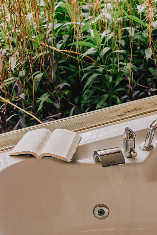 Free Relaxing outdoor bath scene with an open book and lush greenery, perfect for unwinding. Stock Photo