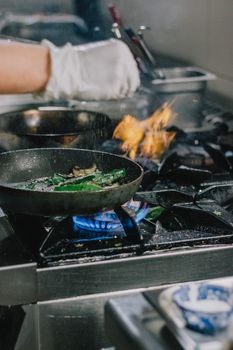 A chef expertly prepares a meal with flames in a modern kitchen setting.