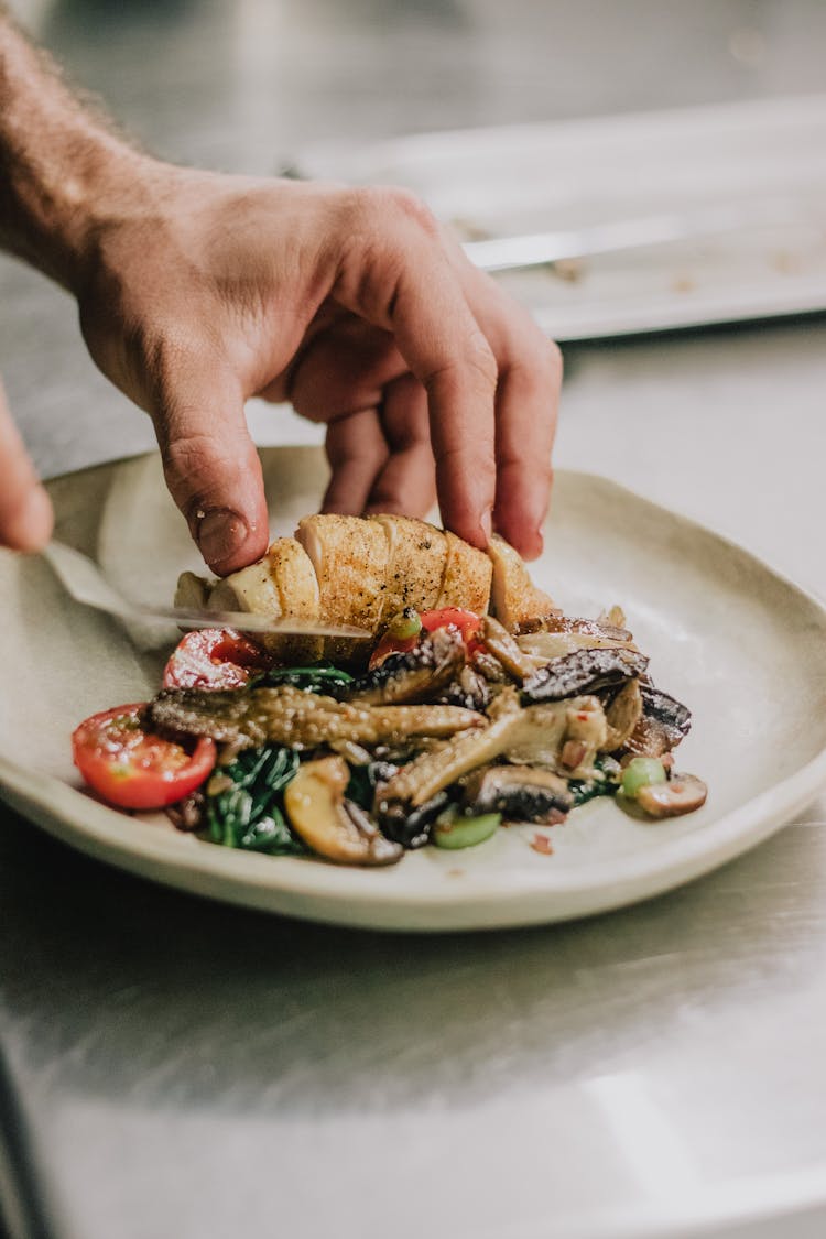 Unrecognizable Hands Cutting Cooked Meat On Plate With Mushroom Salad