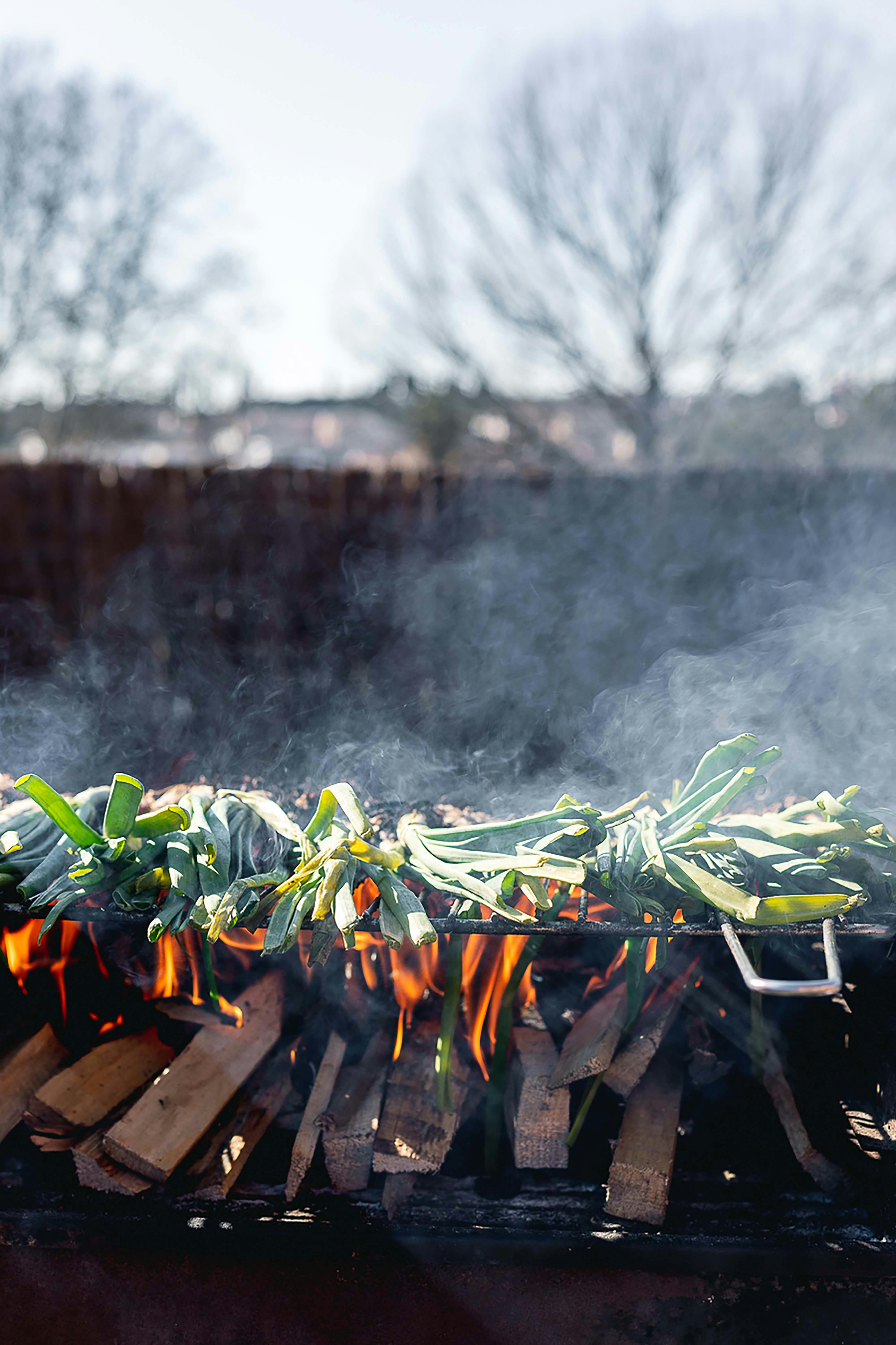 Calçots grilling over open flame barbecue in Barcelona, Spain with smoke rising.