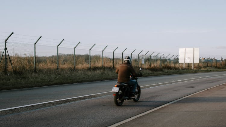 Man In Brown Jacket Riding Motorcycle On The Road