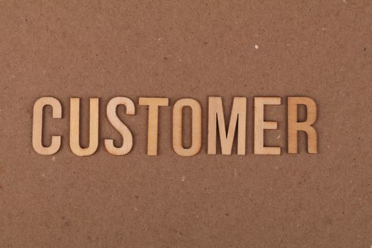 Wooden letters arranged to spell 'customer' on a plain cardboard surface for marketing concept.