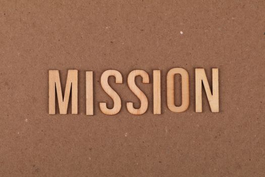 Wooden letters spelling 'MISSION' on textured cardboard background, emphasizing goals and purpose.