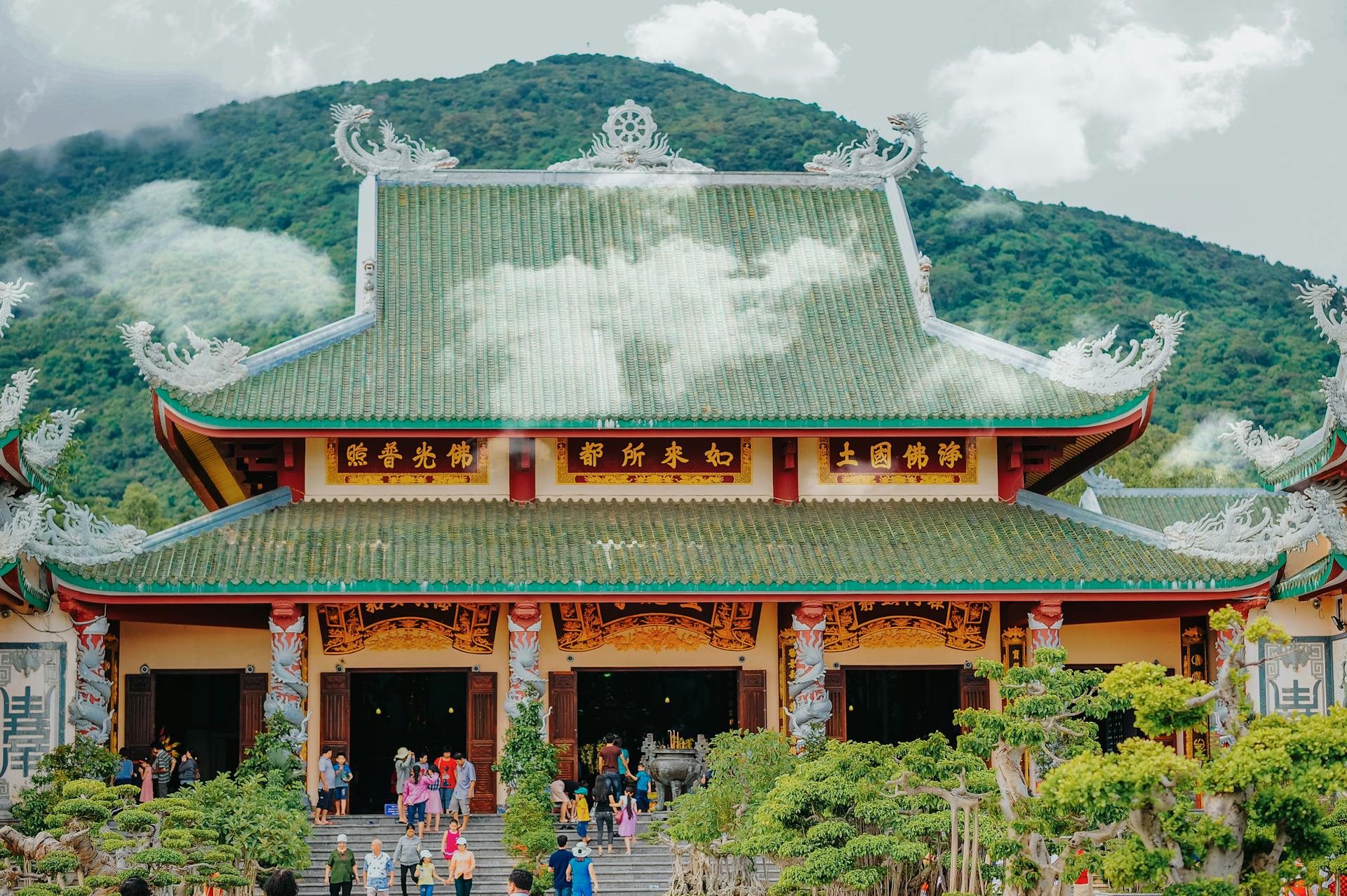 Beautiful traditional Asian temple with green roof and mountainous backdrop.