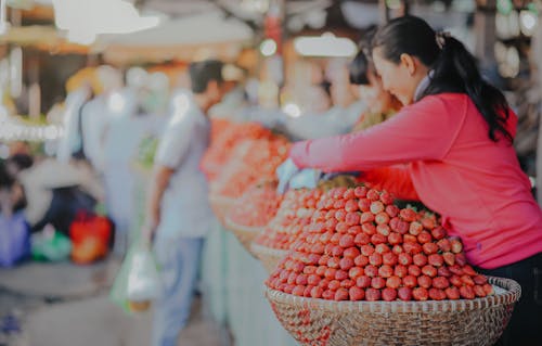 Fotografía Enfoque Diferencial De Una Mujer Con Sudadera Roja De Pie Detrás De Una Cesta Llena De Frutas