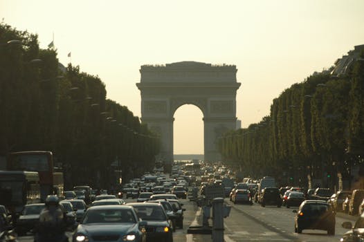 Busy traffic scene captured on a sunny day at the iconic Arc de Triomphe in Paris, France.