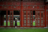 在越南顺化，一位头戴越南帽的女子站在一扇华丽的红门旁