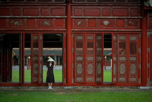 在越南顺化，一位头戴越南帽的女子站在一扇华丽的红门旁