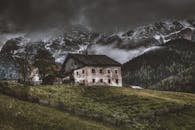 在暴风雨的天空下，一座古宅矗立于戏剧性的山峦背景中