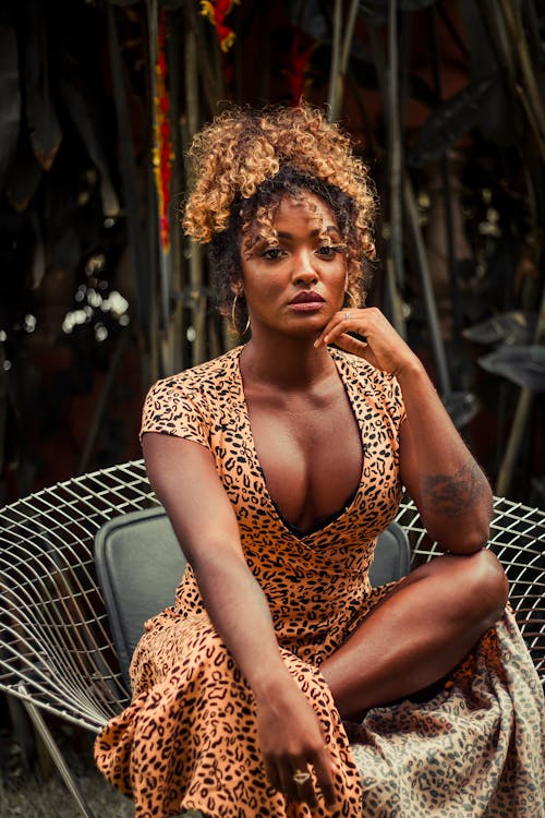 Woman with Curly Hair in Animal Print Dress Sitting on Chair