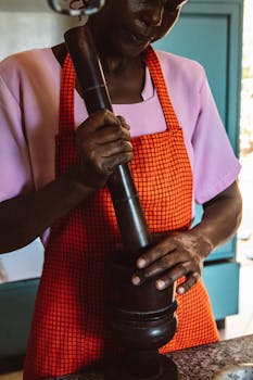 A senior African American woman prepares food with a mortar and pestle in the kitchen.