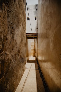 A narrow, sunlit alley casts dramatic shadows between weathered walls.